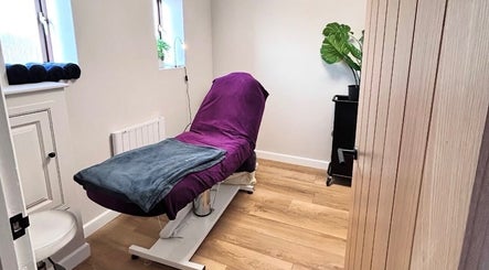 Elegant treatment room at Beauty by Claudie, Gamlingay, England, GB, featuring a plush purple bed and plants.
