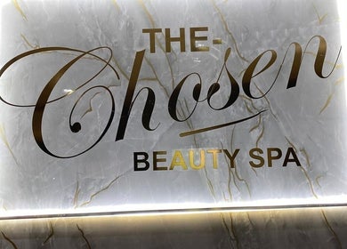Illuminated signage of The Chosen Beauty Spa, Sandton, Gauteng, ZA, in elegant gold font on marble backdrop.