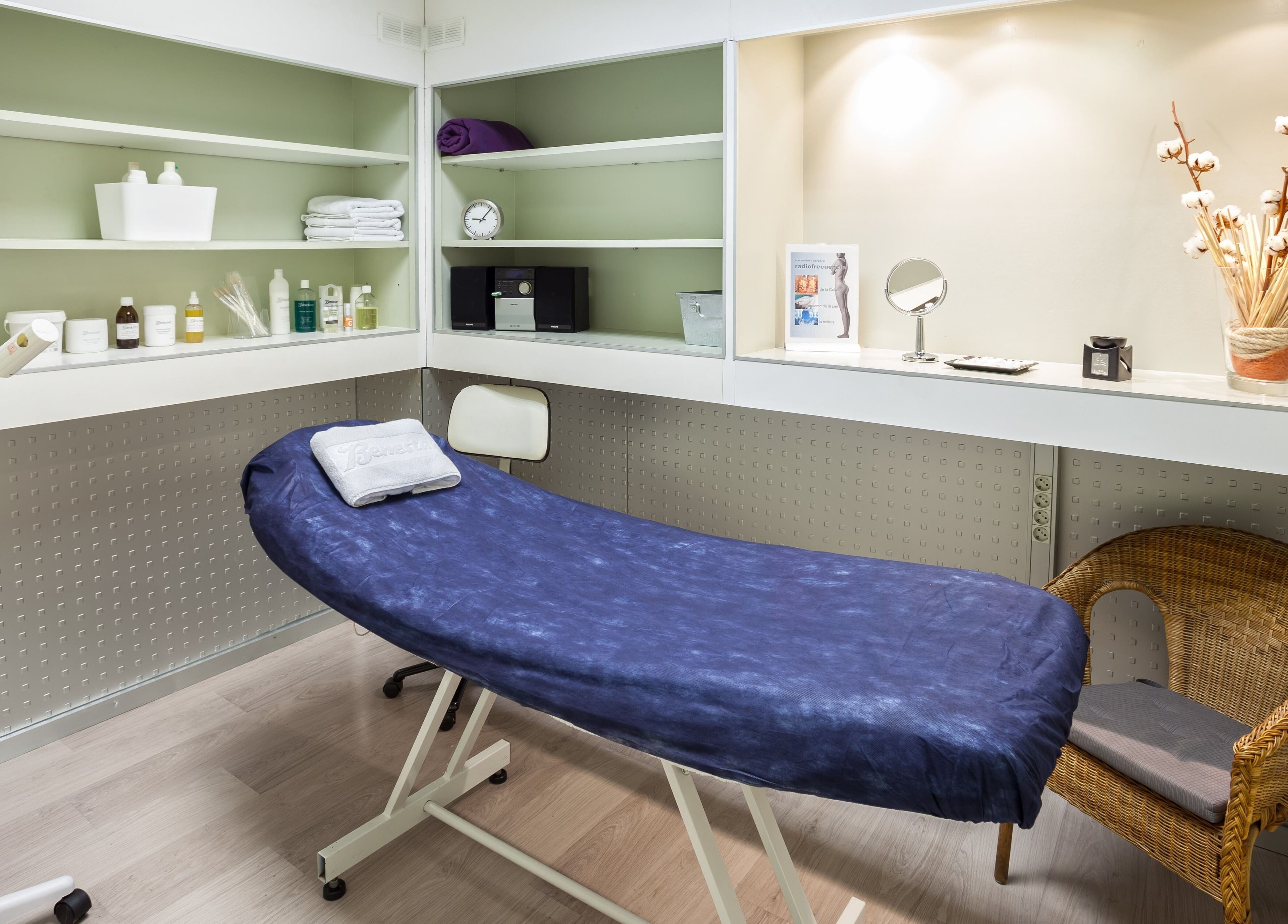 Sala de tratamiento en Benestar Calvet, Barcelona, Catalunya, ES, con camilla azul y estantes con productos.