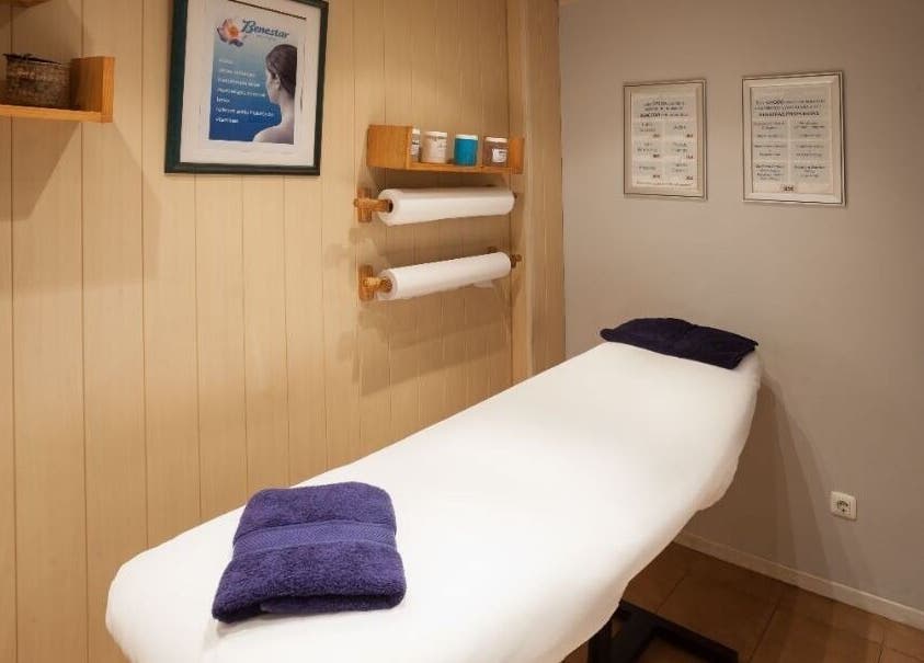 Sala de masaje en Benestar Sarrià, Barcelona, Catalunya, ES, con camilla blanca y toallas púrpuras.