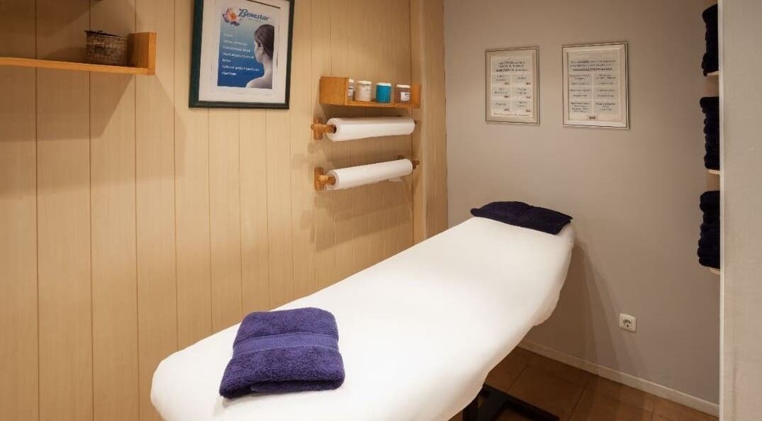 Sala de masaje en Benestar Sarrià, Barcelona, Catalunya, ES, con camilla blanca y toallas púrpuras.