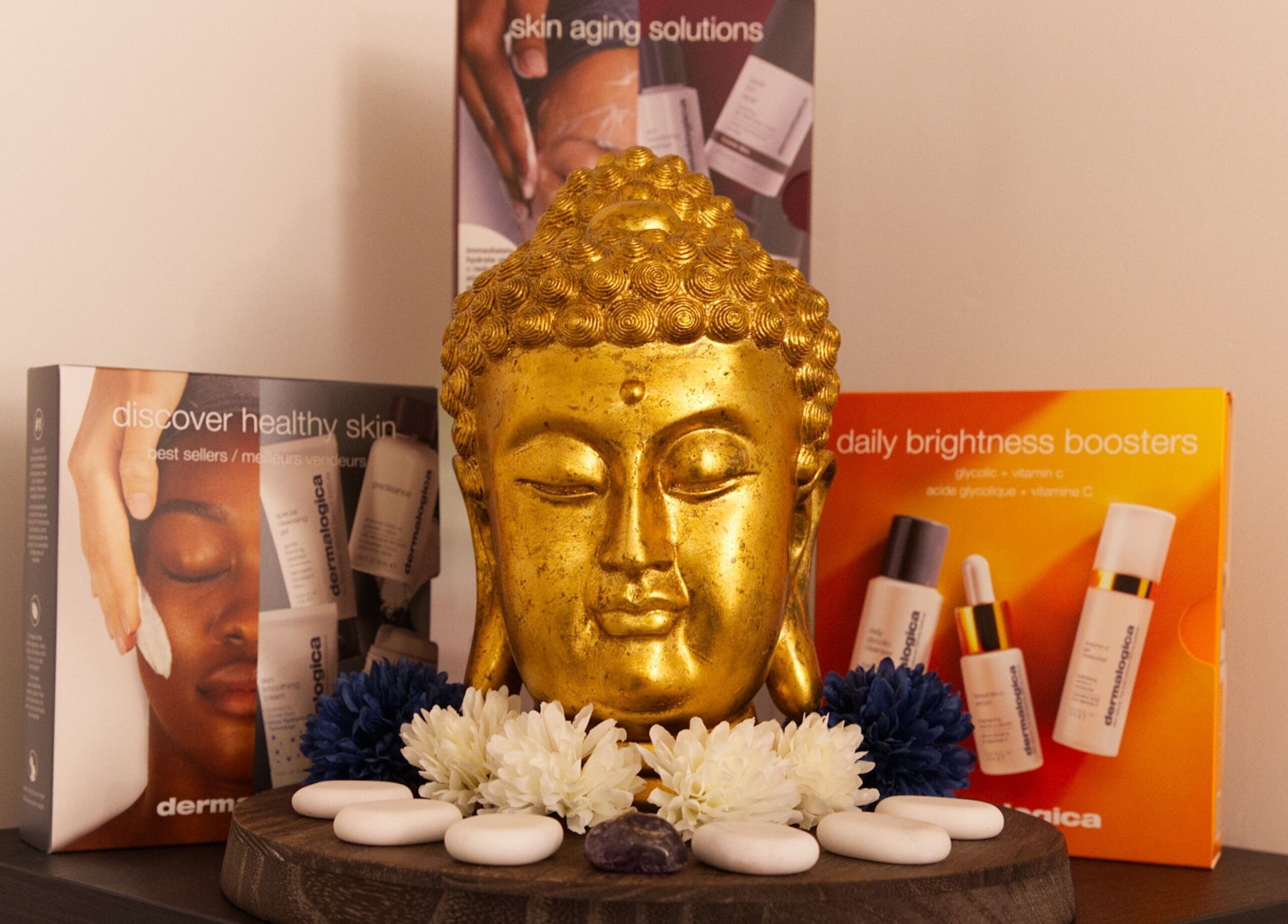 Golden Buddha head at TMB Beauty, Brighton GB, surrounded by skincare products and flowers.