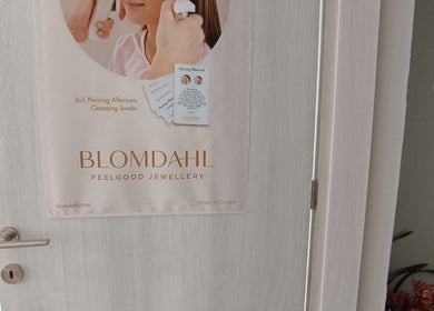 Πόστερ Blomdahl στην πόρτα του The F.L.Y. Room, Γιάννουλη, GR. Διαφημίζει κοσμήματα και φροντίδα piercing.