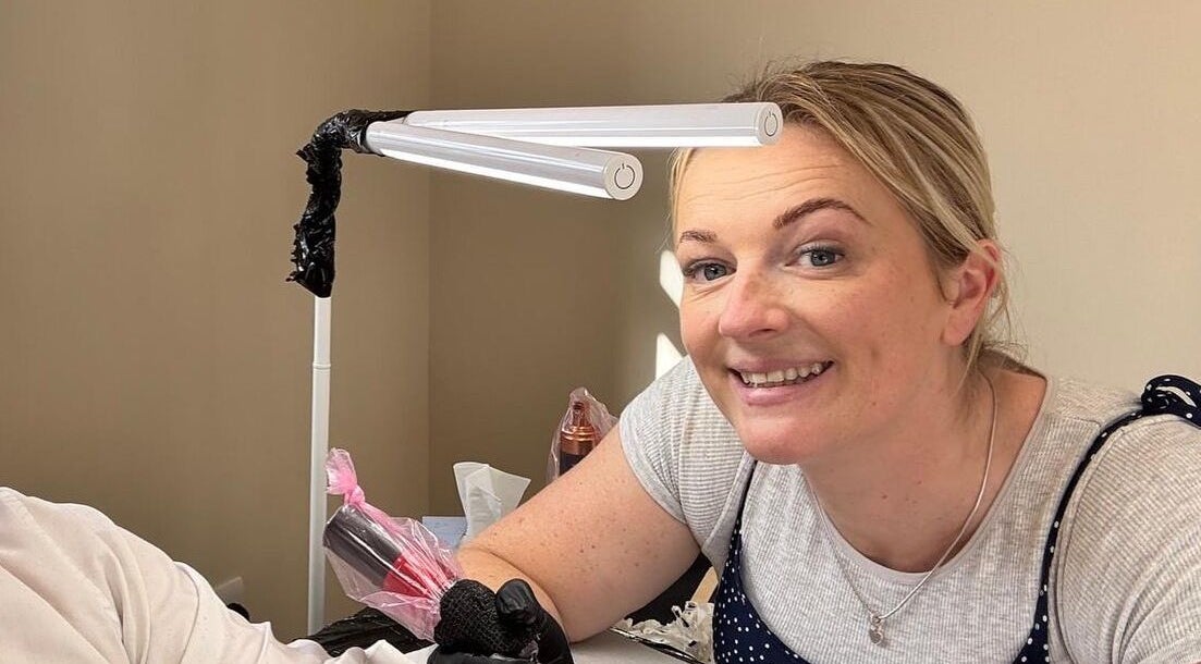 Tattoo artist smiling during a session at Inklet studio, Dunmow, England, GB.