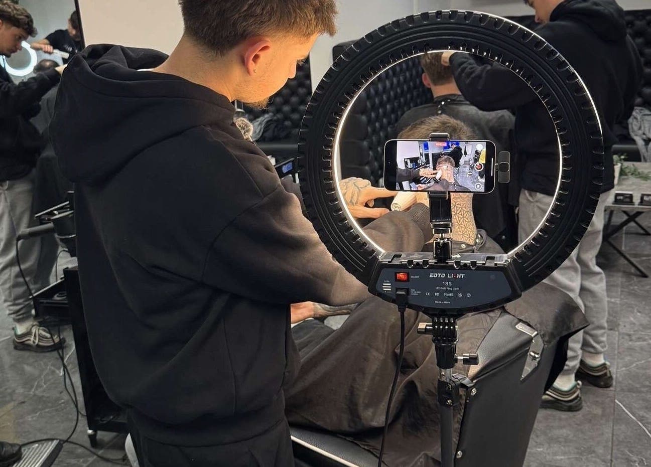 Barber styling hair at Charles Maclean Elite, Bridgwater, England, GB with a camera setup showing the process.