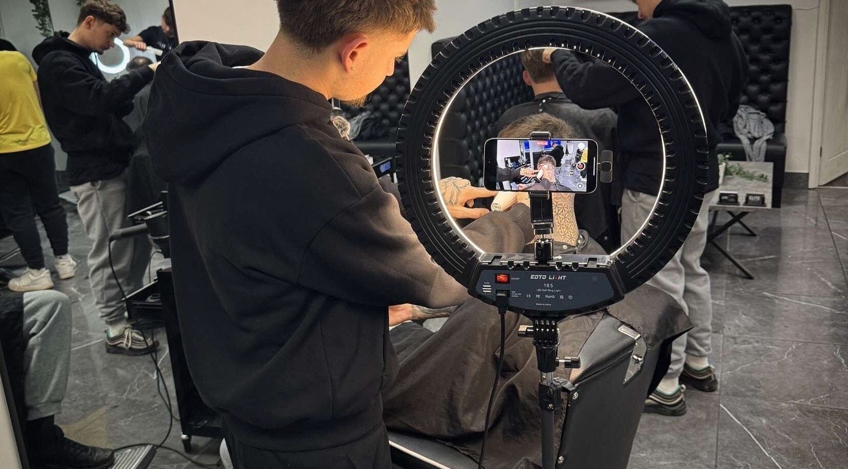 Barber styling hair at Charles Maclean Elite, Bridgwater, England, GB with a camera setup showing the process.