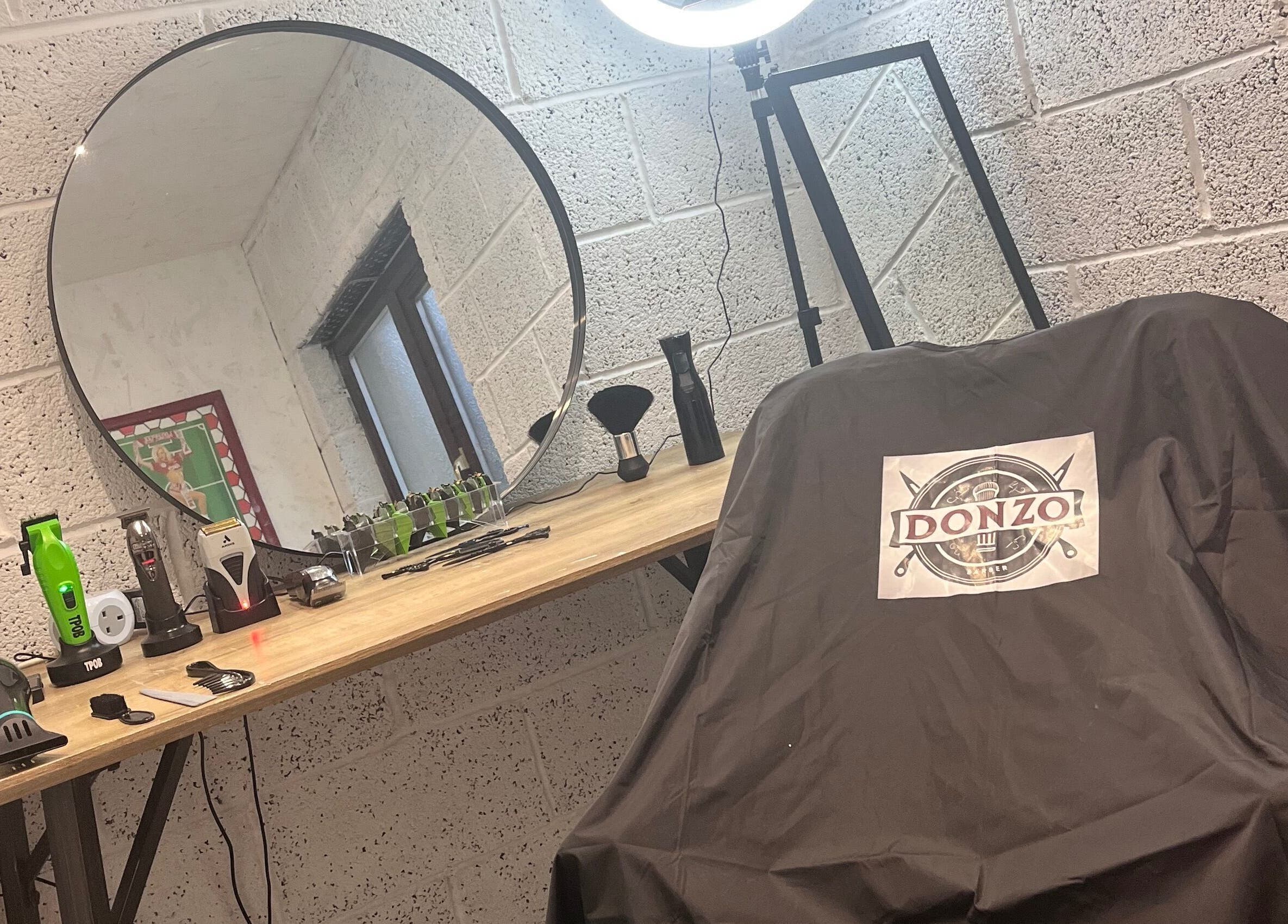 Modern barber station at Donzos_cuts, Pembroke, Wales, GB featuring tools, a large mirror, and branded chair cover.