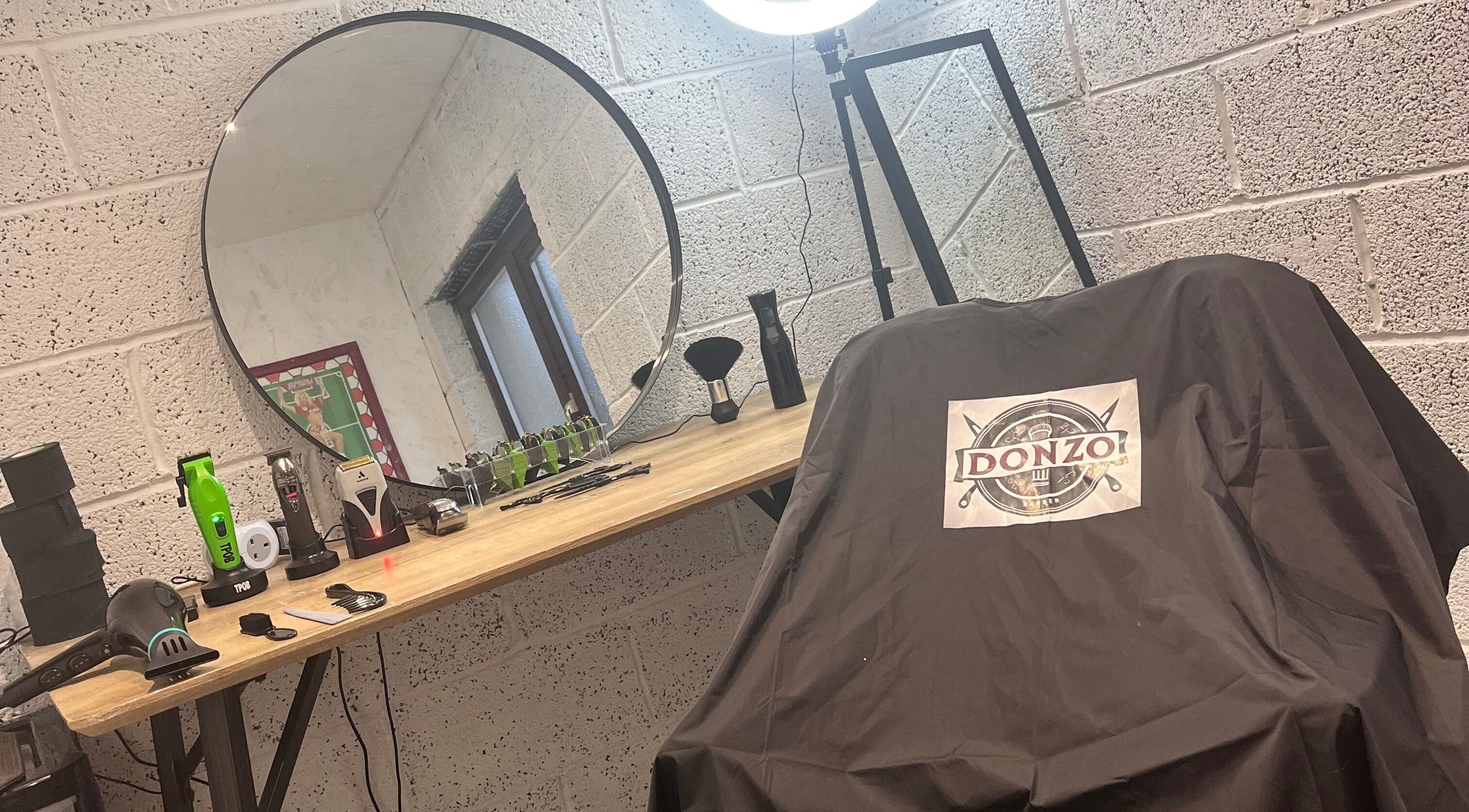 Modern barber station at Donzos_cuts, Pembroke, Wales, GB featuring tools, a large mirror, and branded chair cover.