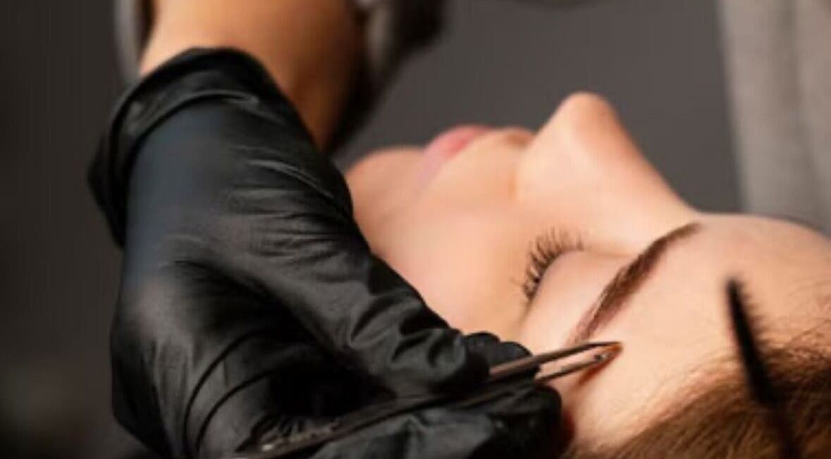Eyebrow shaping at Lash & Brow Haven, Brisbane, Queensland, AU. A hand tweezes a client's eyebrow.