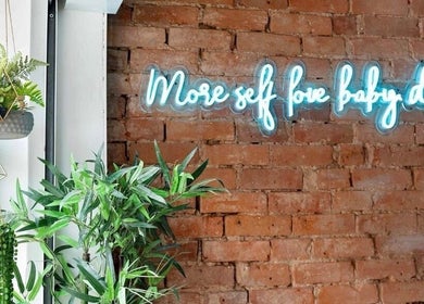 Modern decor at Styled by Beth, Bromsgrove, England, GB features a neon sign and lush greenery against brick wall.