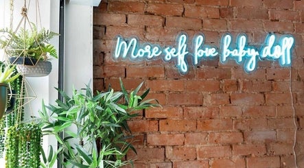 Modern decor at Styled by Beth, Bromsgrove, England, GB features a neon sign and lush greenery against brick wall.