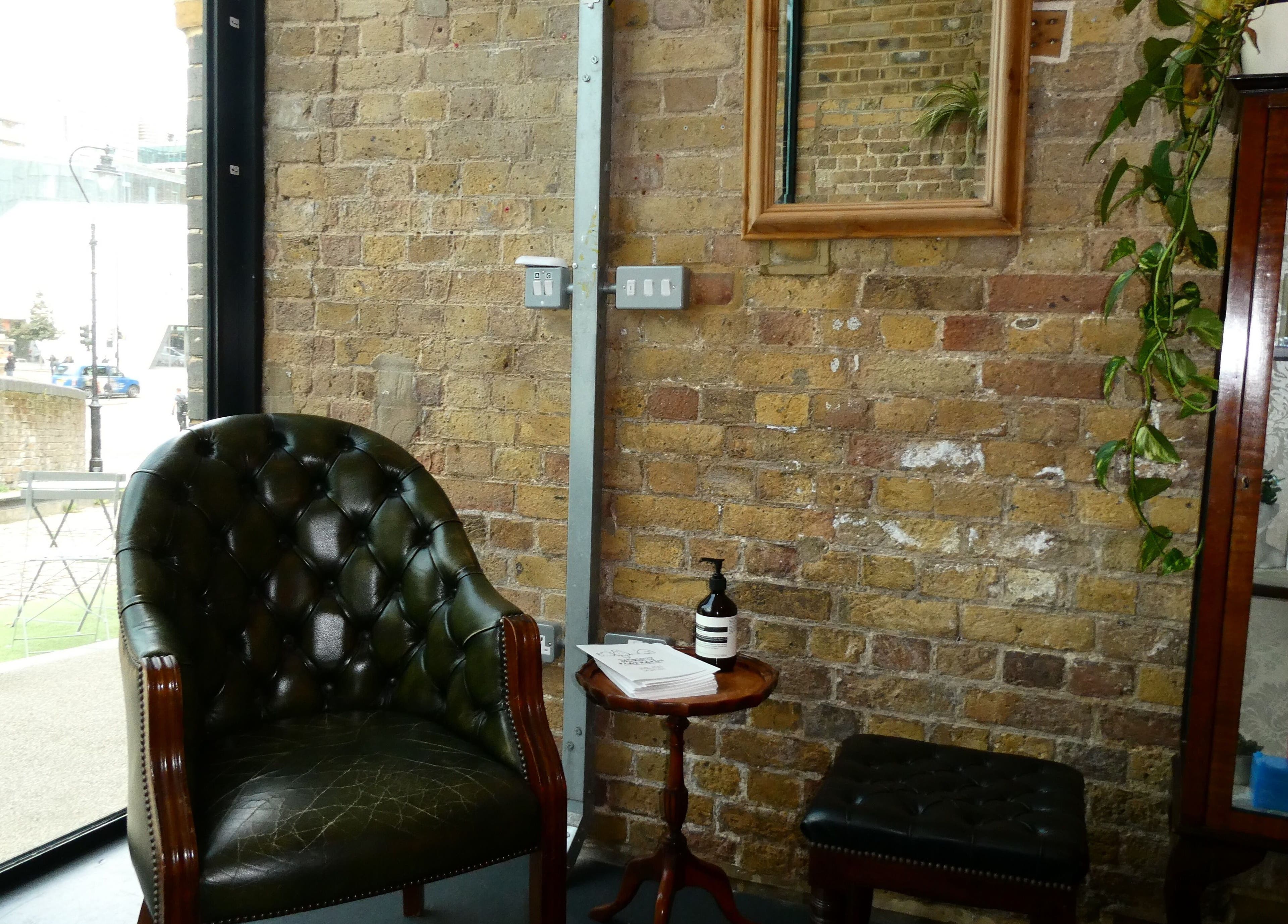 Elegant waiting area at Artworks96s | At Quark Hair Studio, London, England, GB with vintage chair and brick wall.