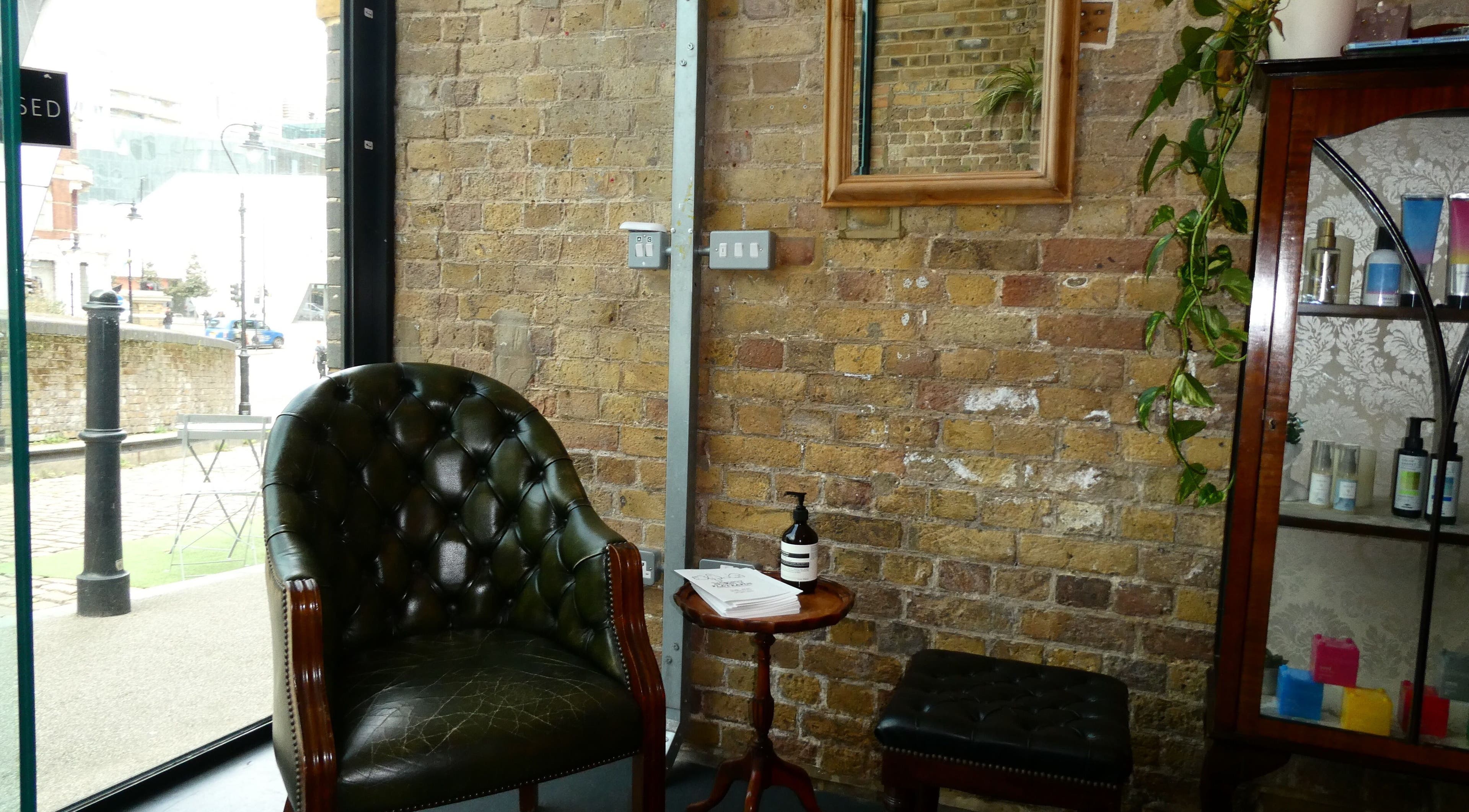 Elegant waiting area at Artworks96s | At Quark Hair Studio, London, England, GB with vintage chair and brick wall.