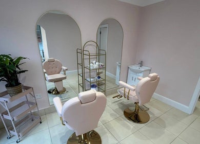 Elegant salon interior at Rose Gold Hair & Beauty in Hounslow, England, GB featuring chic pink chairs and a mirror.