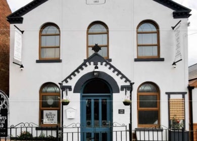 Front view of The Sinners Social Club, a historic venue in Ilkeston, England, GB with arched windows and blue door.