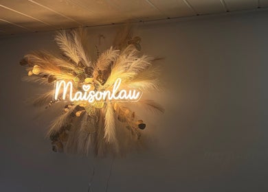 Enseigne lumineuse de MaisonLau, Vieux-Thann, Grand Est, FR, entourée de décorations florales.