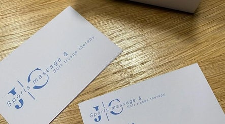 JC Sports Massage and Soft Tissue Therapy business cards on a wooden table in Chesterfield, England, GB.