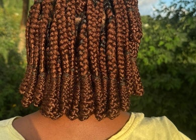 Intricate braids showcased at Hair .Byann, Kingstown, VC amidst lush greenery.