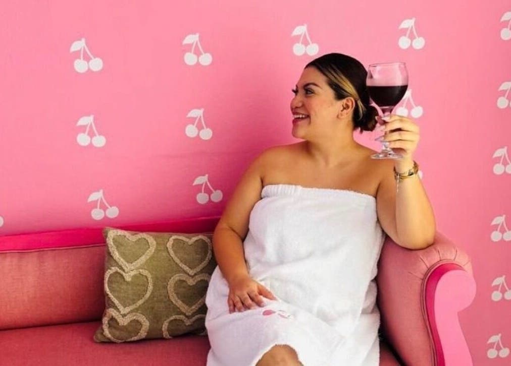 Mujer relajada en Cherry Spa & Skin Care, Alajuela, disfrutando de un vino en un sofá rosa.