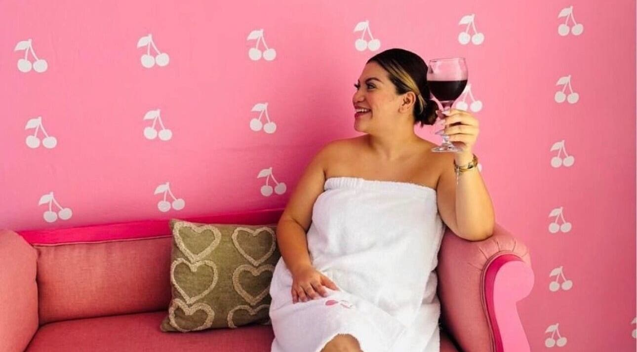 Mujer relajada en Cherry Spa & Skin Care, Alajuela, disfrutando de un vino en un sofá rosa.