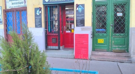 Anna fodrászat piros ajtóval Budapest, Magyar, HU címen. Található zöld növényekkel az előtérben.