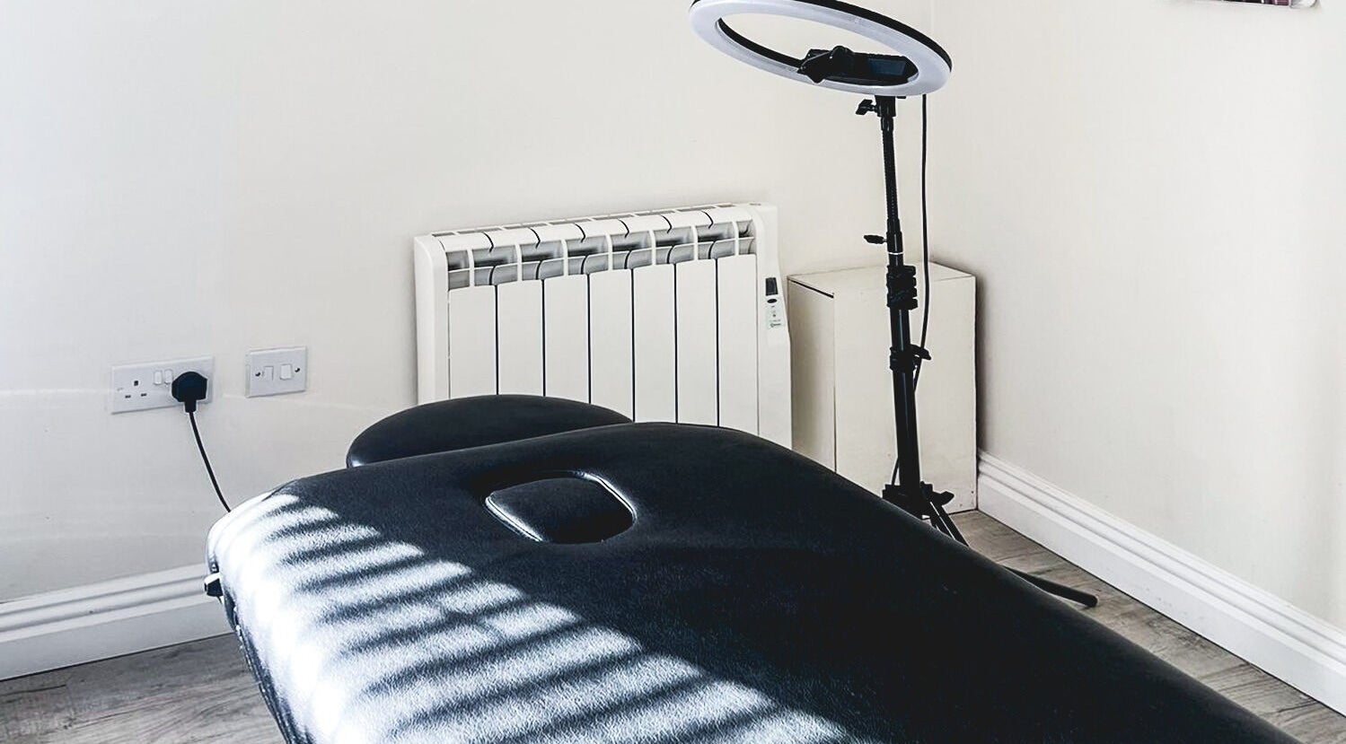Treatment room at The Brow Rehab, Little Lever, England, GB with a black massage table and ring light.