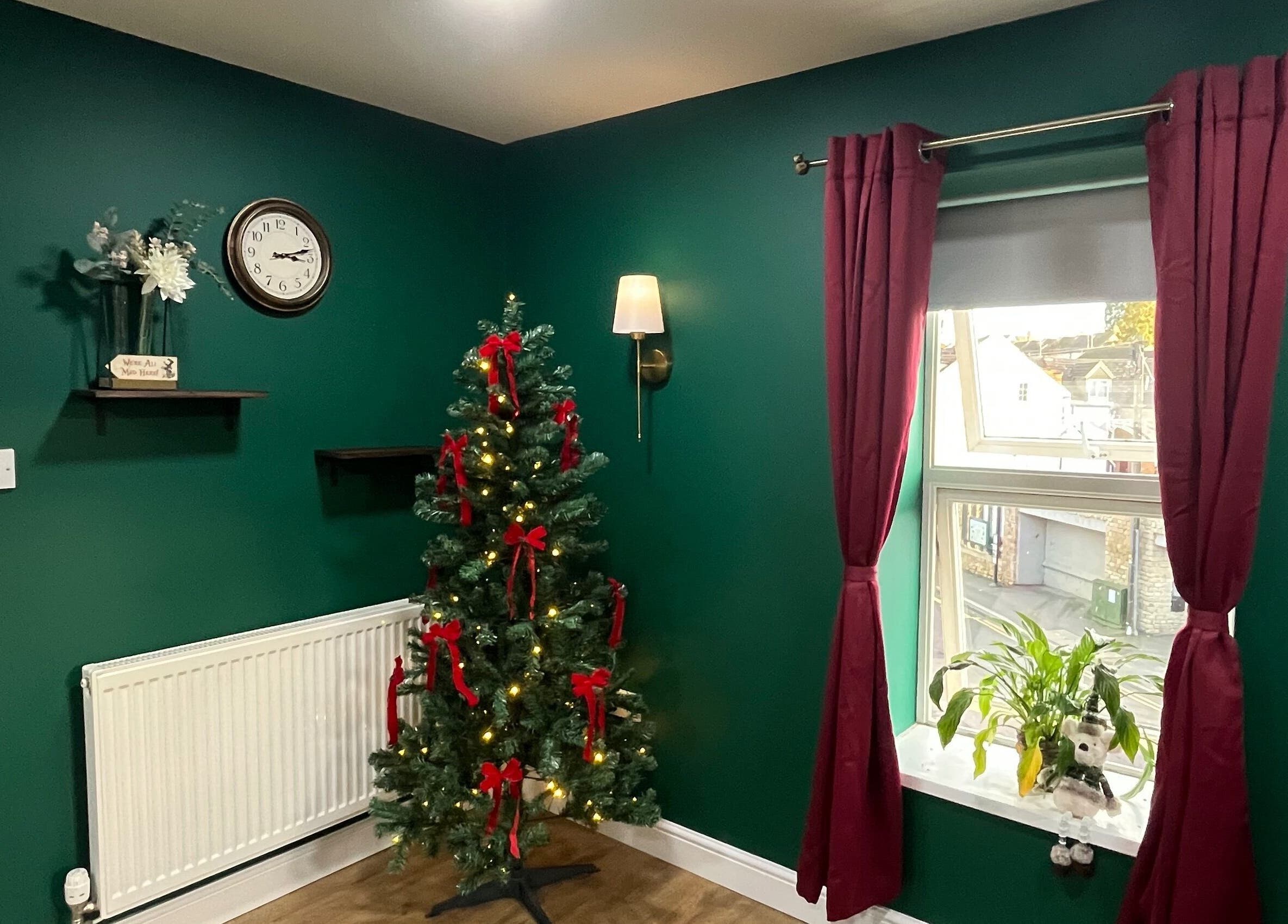 Festive corner with Christmas tree at The Hatters Beauty Room, Finedon, England, GB, featuring green walls and red curtains.