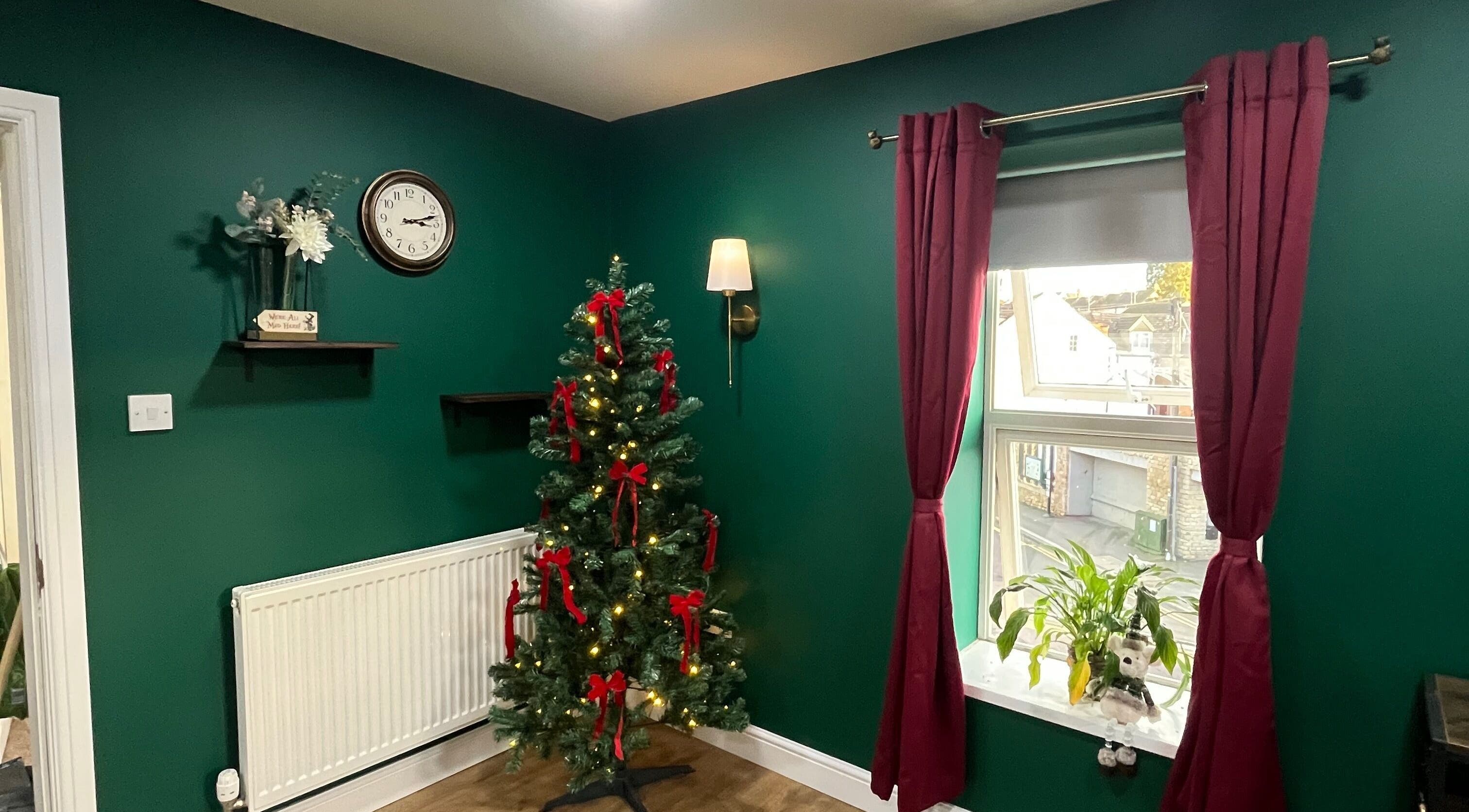 Festive corner with Christmas tree at The Hatters Beauty Room, Finedon, England, GB, featuring green walls and red curtains.
