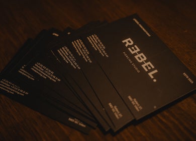 Stapel visitekaartjes met logo van REBEL. Piercing Studio, Uden, Noord-brabant, NL op houten tafel.