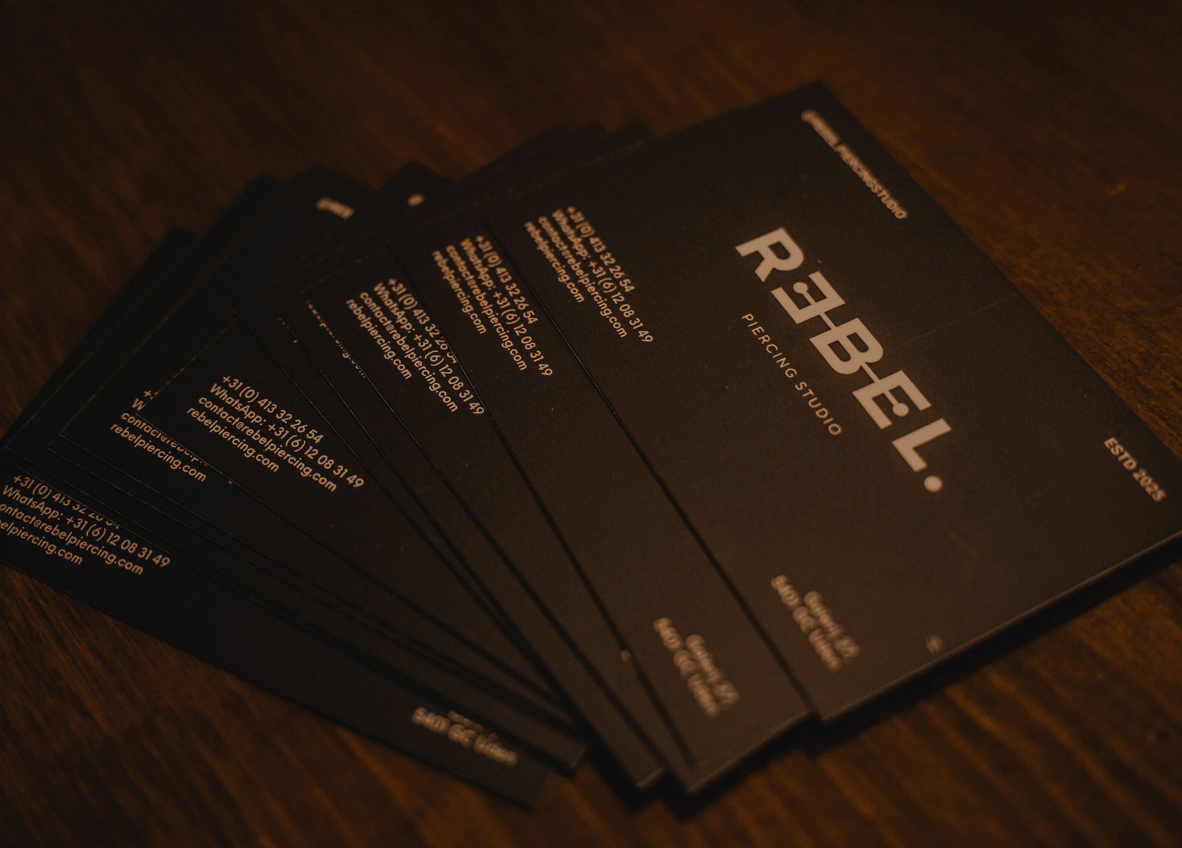 Stapel visitekaartjes met logo van REBEL. Piercing Studio, Uden, Noord-brabant, NL op houten tafel.