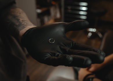 Een professionele piercer in REBEL. Piercing Studio, Uden, Noord-brabant, NL, toont een kleine zilveren ring met zwarte handschoenen.