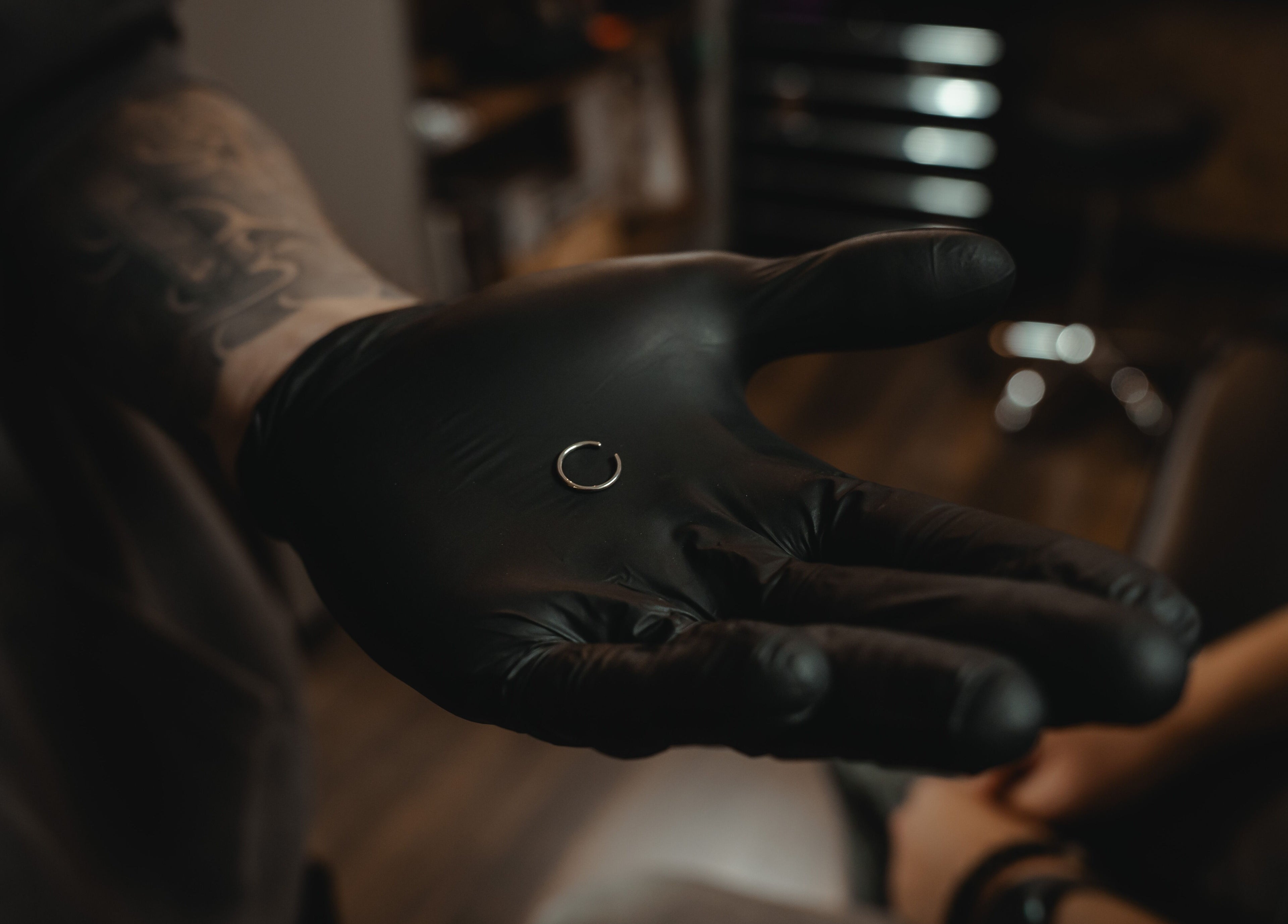 Een professionele piercer in REBEL. Piercing Studio, Uden, Noord-brabant, NL, toont een kleine zilveren ring met zwarte handschoenen.