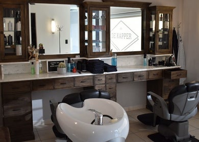 Interieur van De Kapper Elewijt in Zemst, Vlaanderen, BE met moderne kappersstoel en houten meubelen.