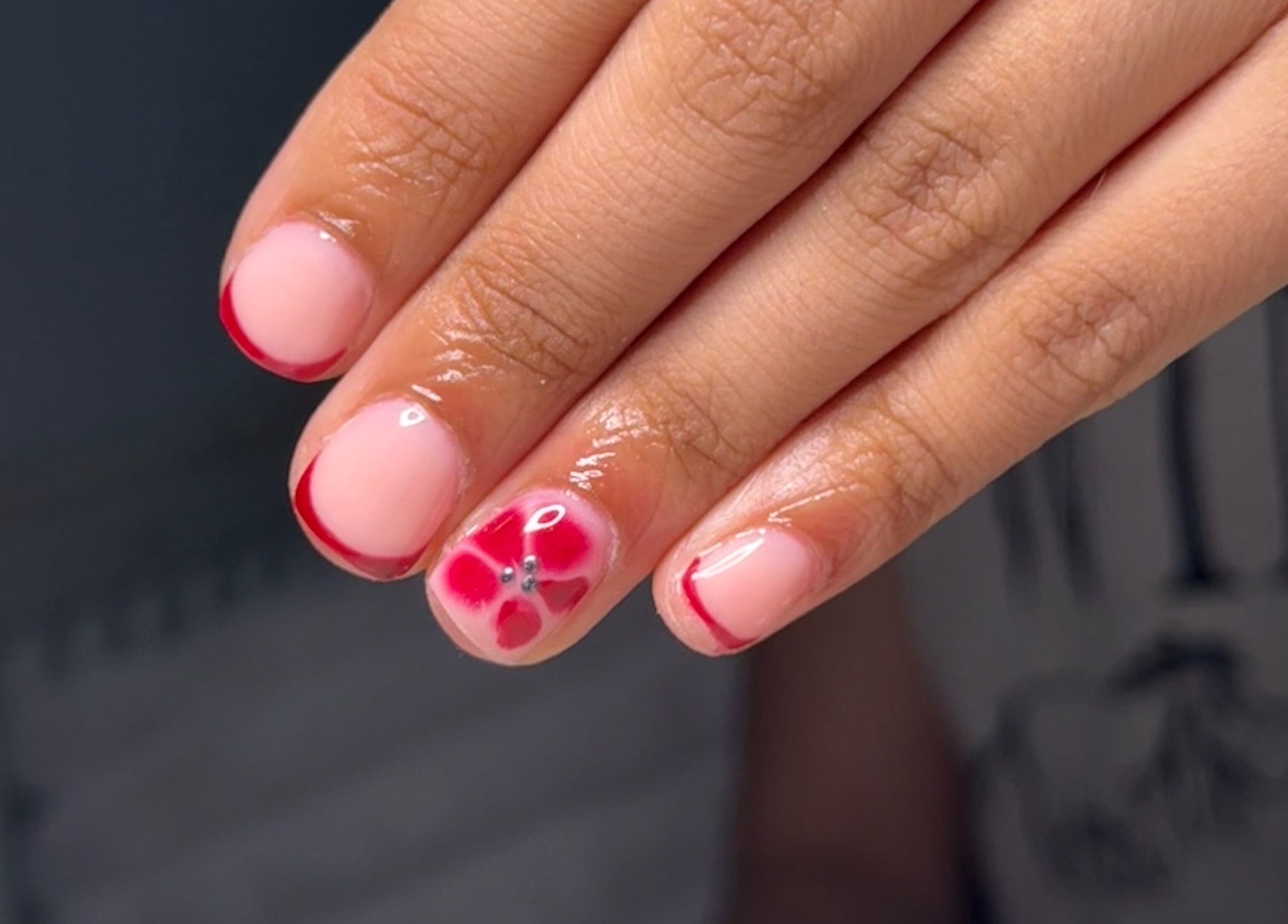 Stylish floral nail art at BySorayah, Birmingham, England, GB. Red tips and flower accent on natural polish.