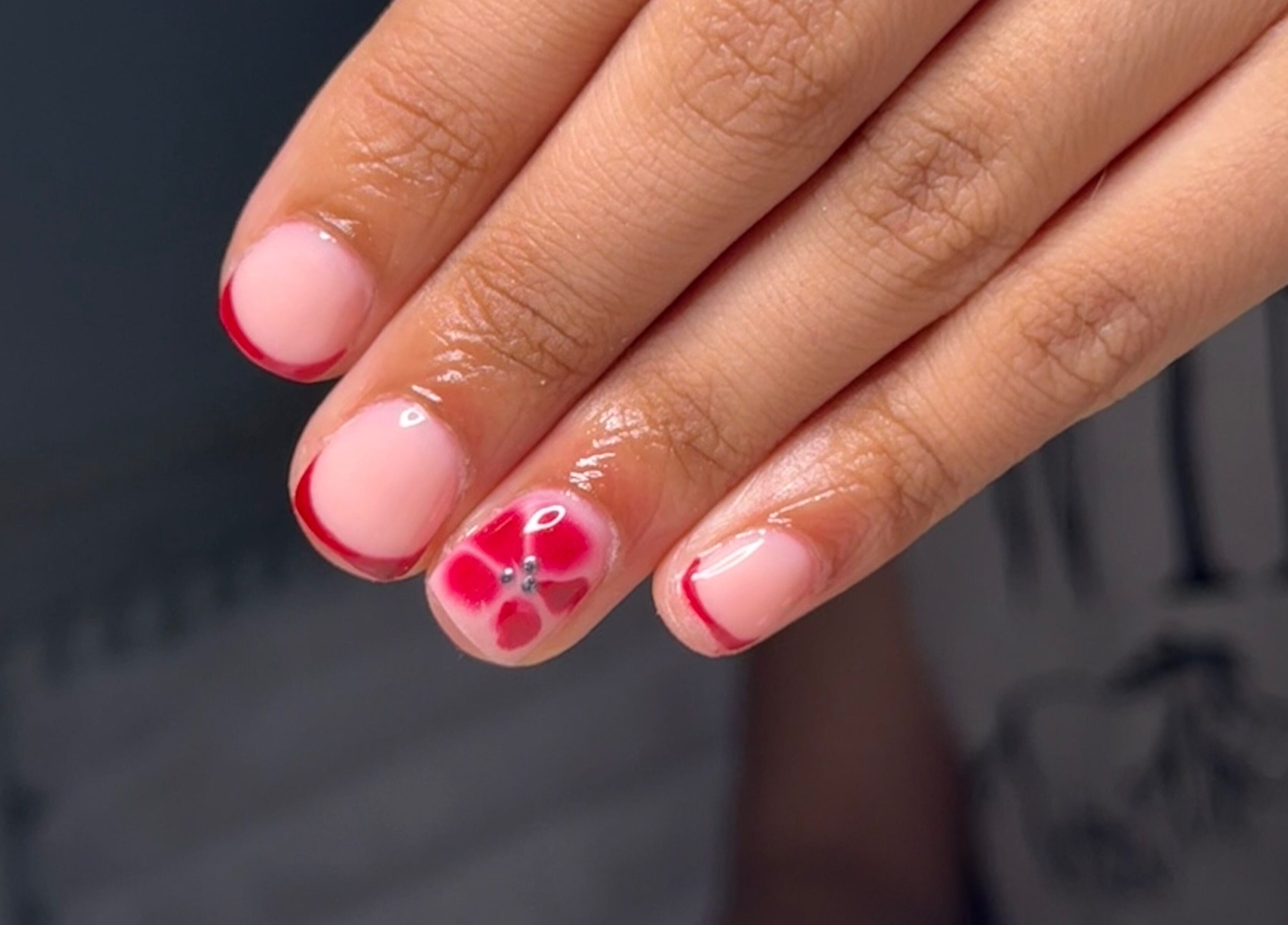 Stylish floral nail art at BySorayah, Birmingham, England, GB. Red tips and flower accent on natural polish.