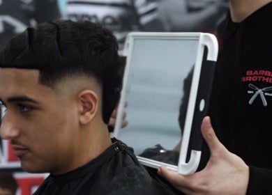 Customer at Barber Brothers in Cronulla, New South Wales, AU showing off a fresh haircut with a handheld mirror.