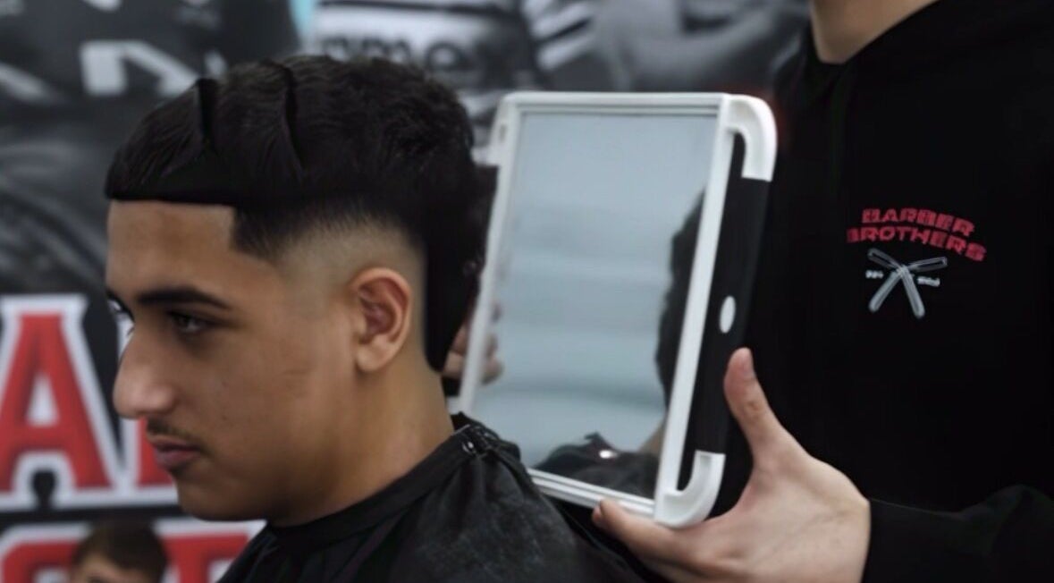 Customer at Barber Brothers in Cronulla, New South Wales, AU showing off a fresh haircut with a handheld mirror.