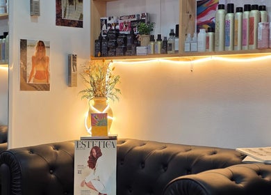 Zona de espera de GABO LLOJA HAIR SALÓN AND BEAUTY en Barcelona, Catalunya, ES, con sofás acogedores y productos de belleza.