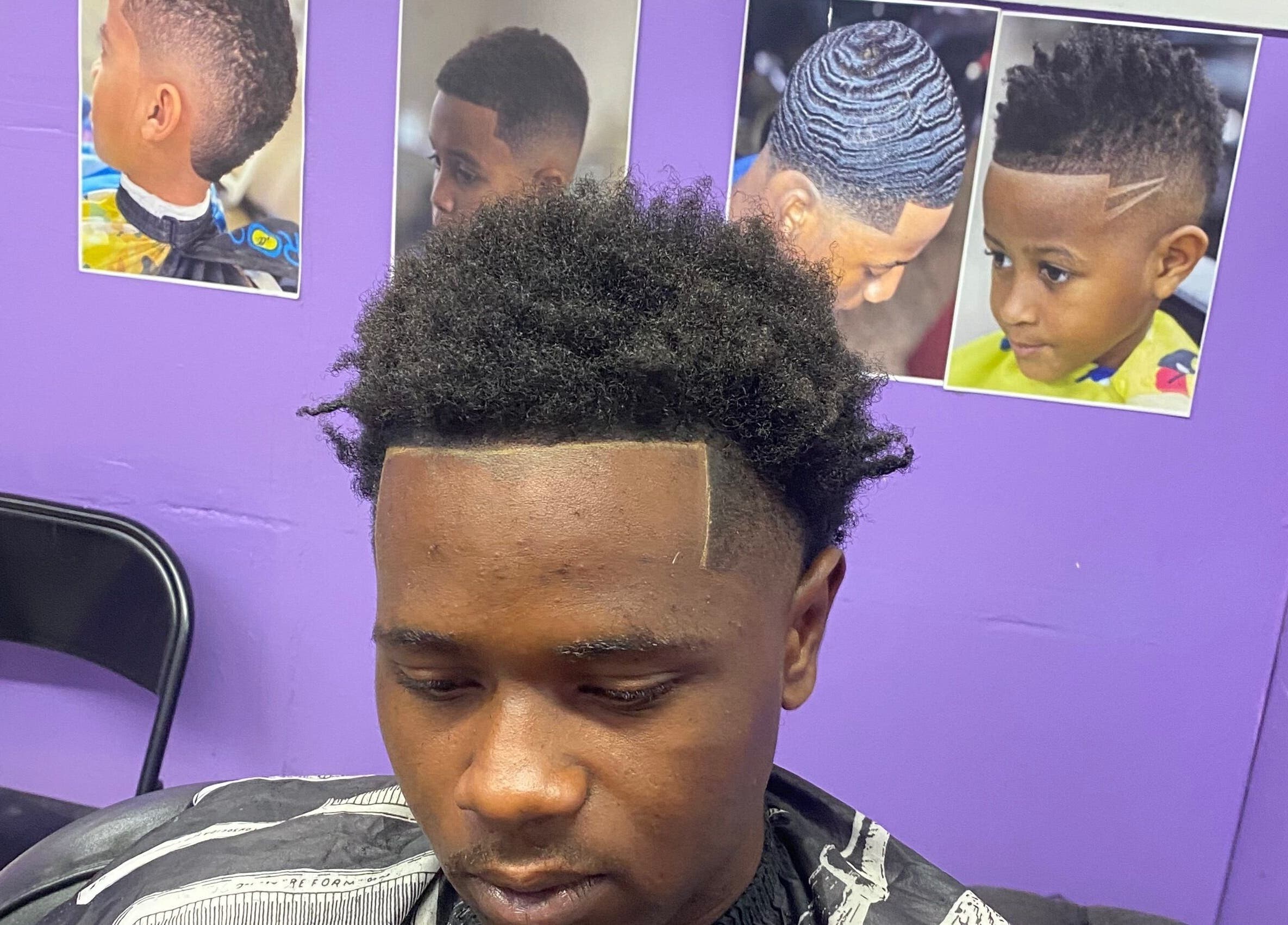 Man with stylish haircut at Dre Cool Cutz, Nassau, New Providence, BS, seated in front of hair style posters.