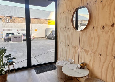 Relaxing corner at Brows & Beauty by Vu in London, England, GB with natural wood decor and a round mirror.