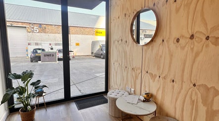Relaxing corner at Brows & Beauty by Vu in London, England, GB with natural wood decor and a round mirror.