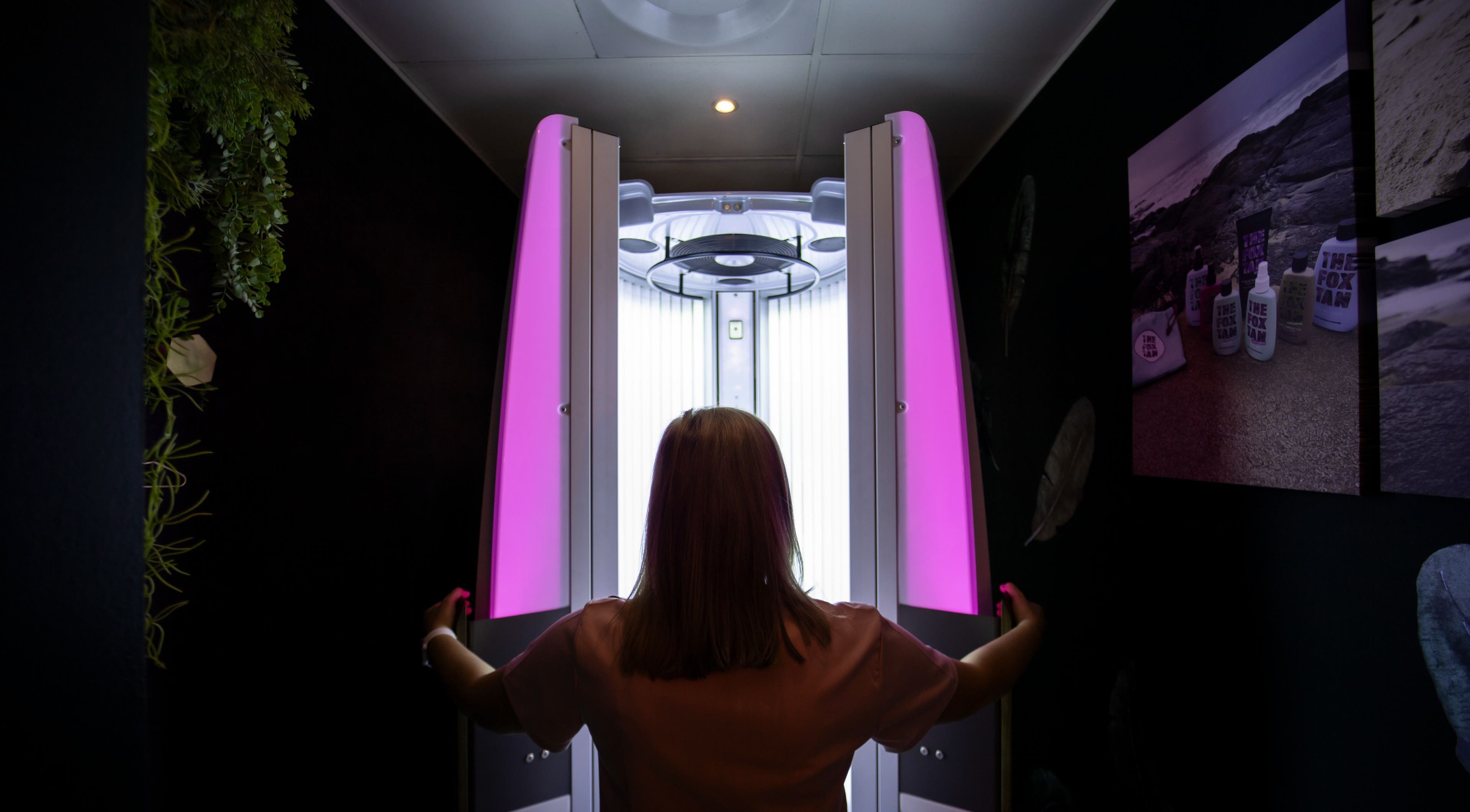 Woman entering a modern tanning booth at Glow Studio, Roodepoort, Gauteng, ZA for a radiant bronzed look.