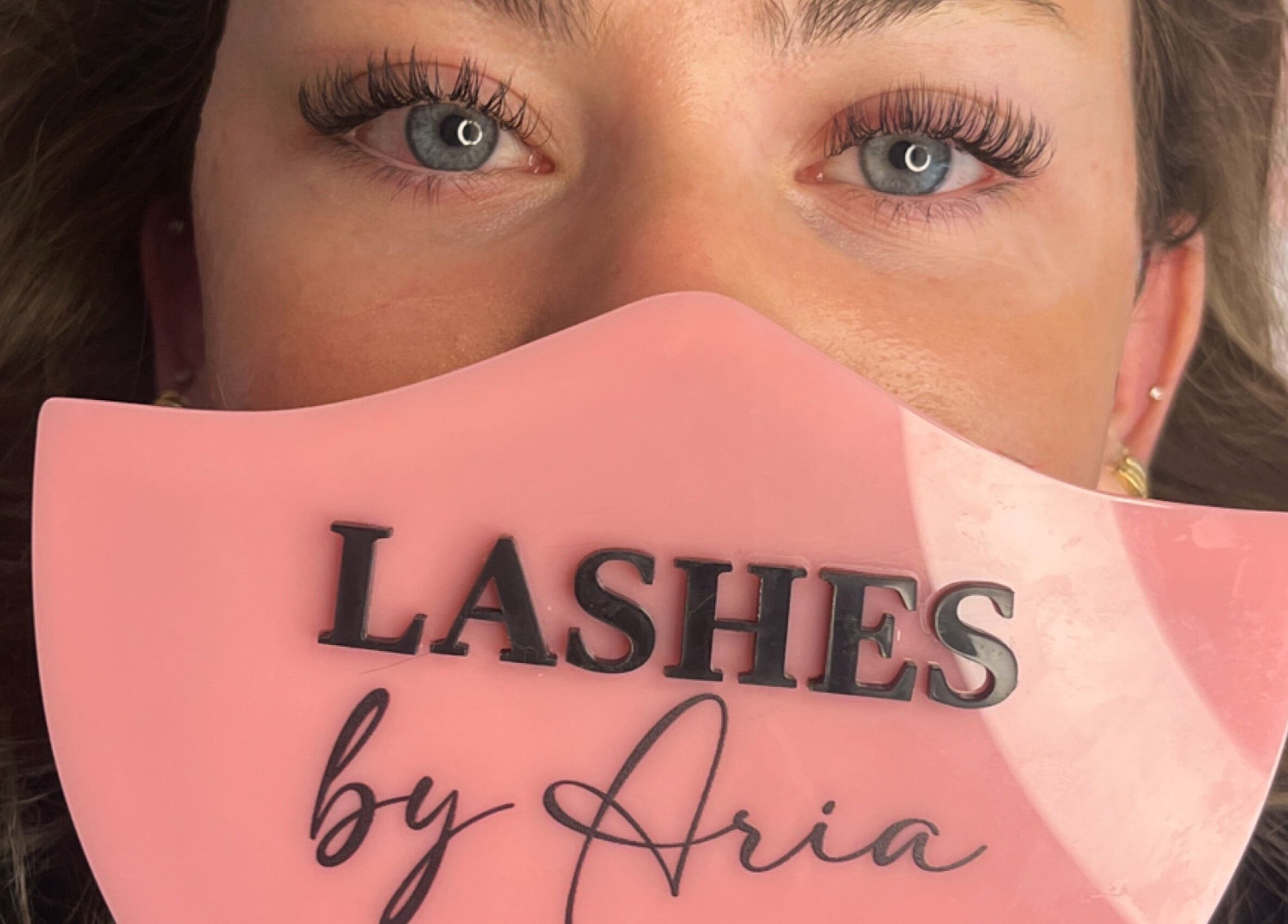 Close-up of elegant eyelashes at Lovely Lash by Aria, Ayr, Ontario, CA on a pink background.