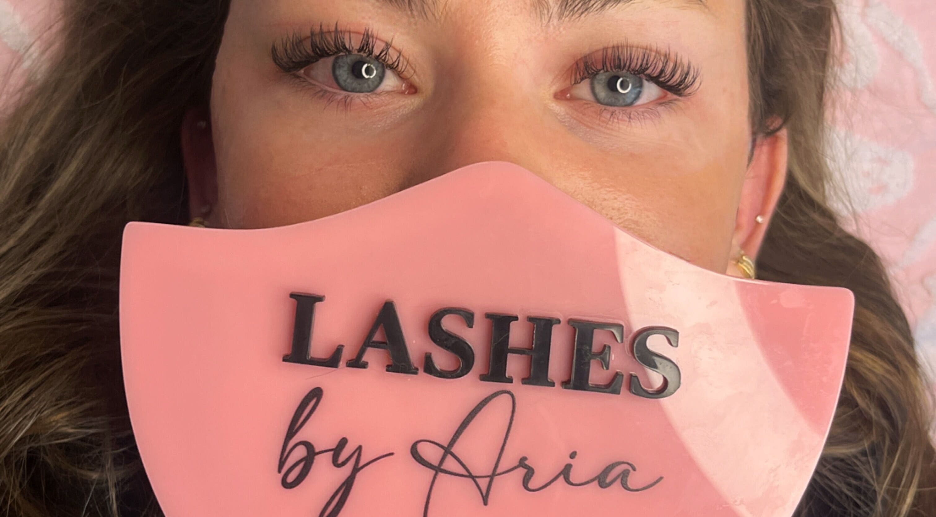 Close-up of elegant eyelashes at Lovely Lash by Aria, Ayr, Ontario, CA on a pink background.