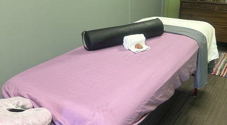 Massage table at Sleepy Koi Bodyworks in Swartz Creek, Michigan, US, with purple sheets and a black bolster.