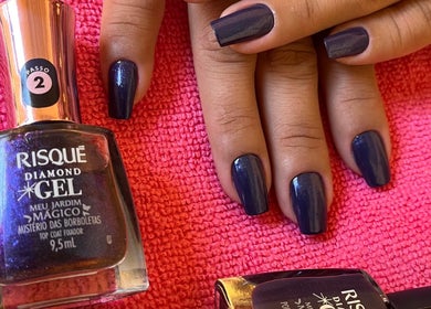 Mãos com esmalte escuro na Toque de Mestra, Minas Gerais, BR, sobre toalha rosa.