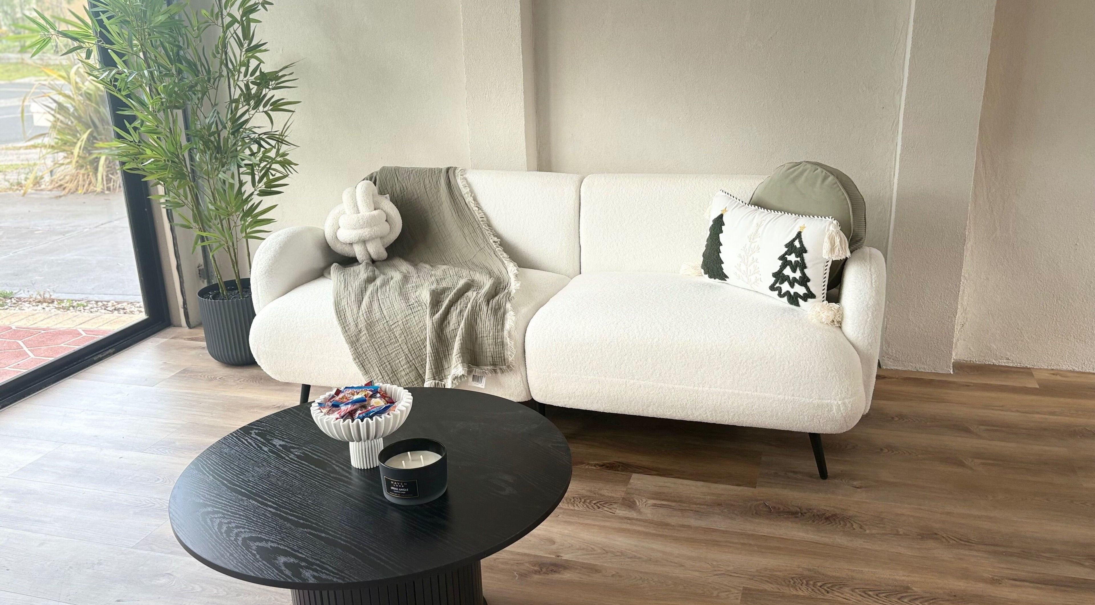 A cozy corner in The KALM Studio, Melbourne, Victoria, AU with a white sofa, throw pillows, and green plant.