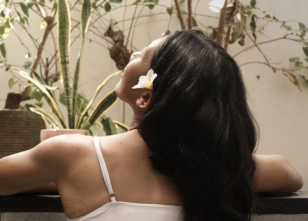 Relaxing at KU Salon & Spa, Nusa Tenggara Barat, woman enjoying serene outdoor bath with flowers.