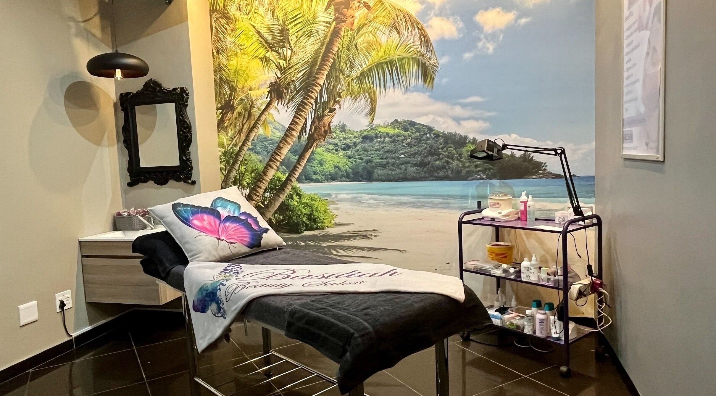 Relaxation room at Basiliah Beauty Salon Tan Can in Pretoria, Gauteng, ZA with tropical beach mural and treatment bed.