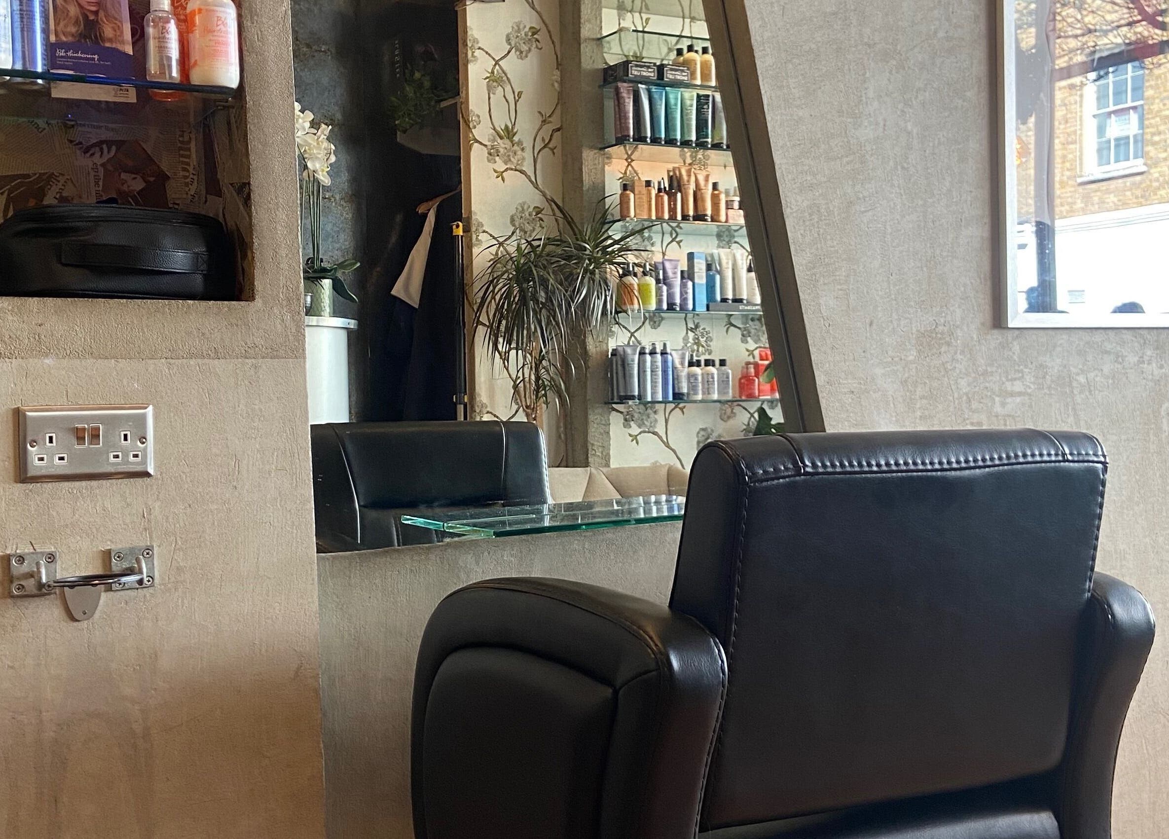 Cozy styling chair and mirror at Transition Salon, London, England, GB; shelves lined with beauty products.